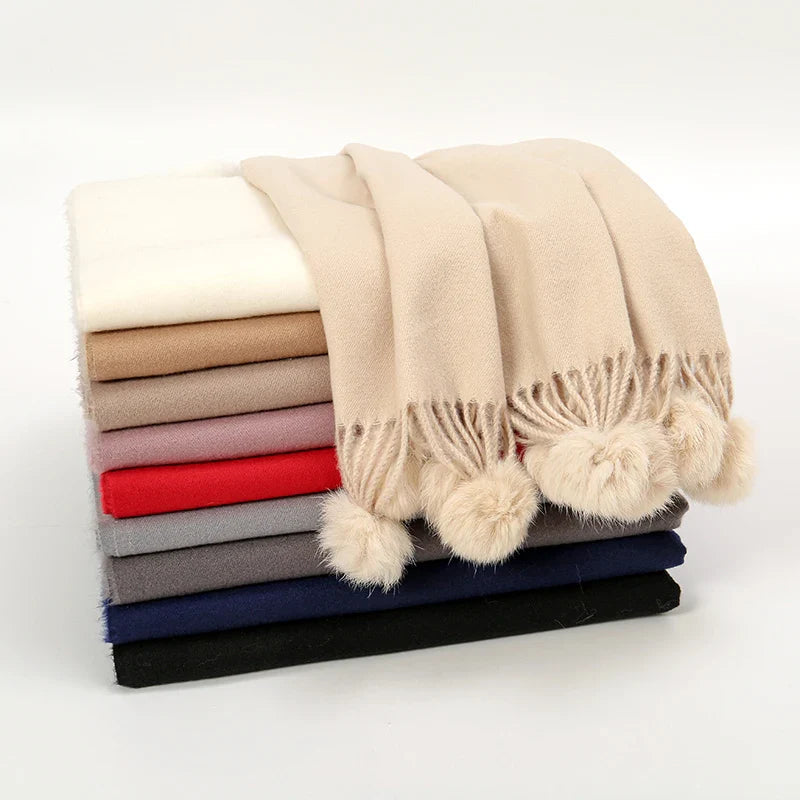 Cashmere scarf featuring pom pom embellishment worn draped