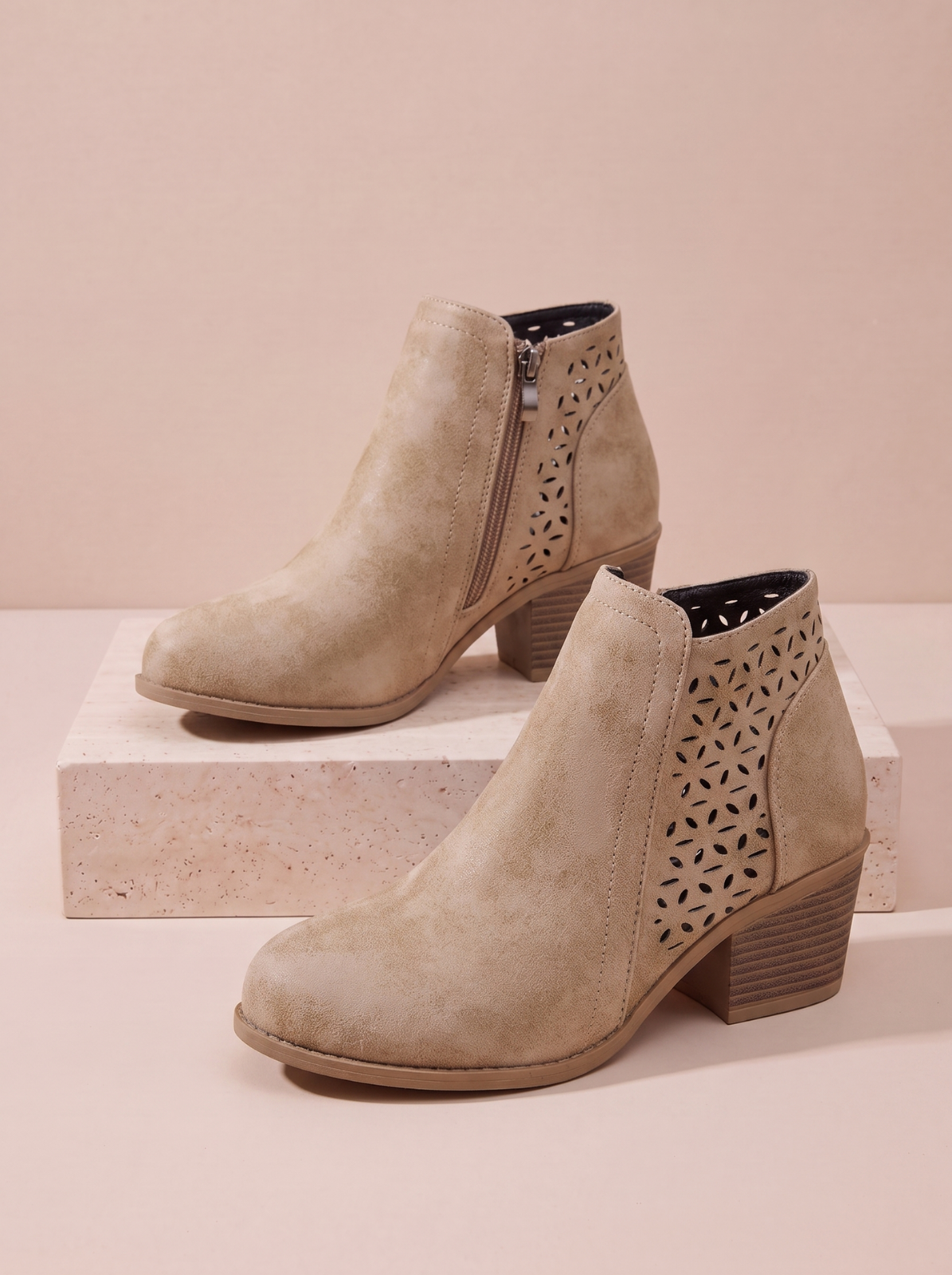 A pair of beige suede ankle boots with geometric laser-cut side 